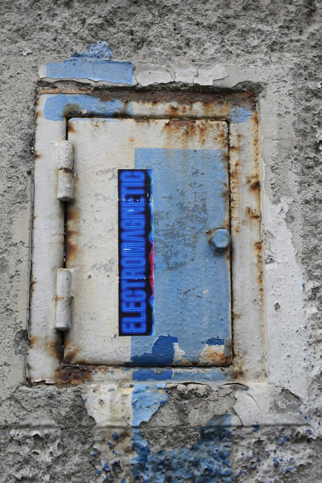 A rusty metal door with an electromagnetic sticker in a concrete wall.